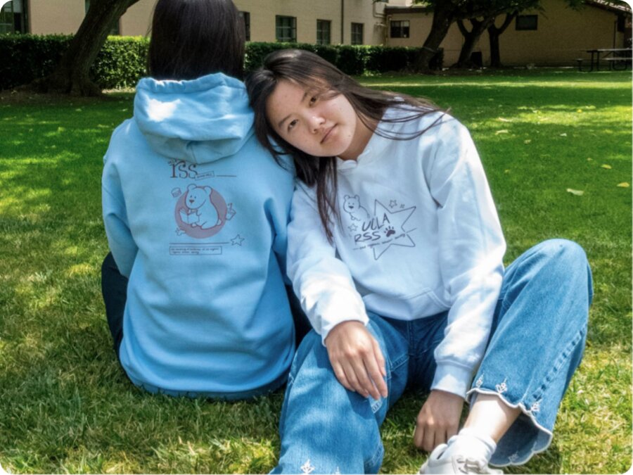 Back view of a model on the grass wearing the white hoodie's bear print