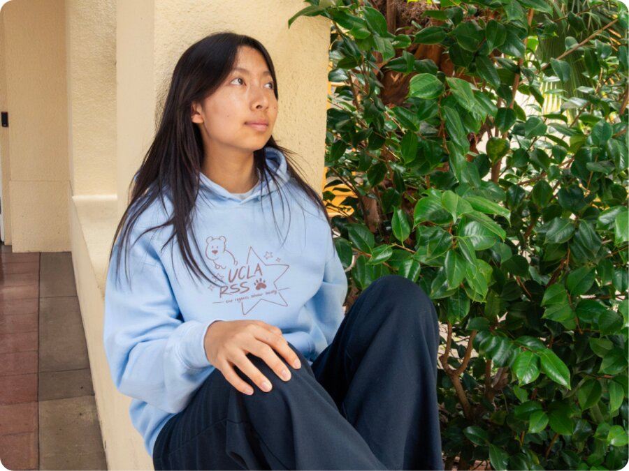 A model in the light-blue hoodie seated against a wall, looking up