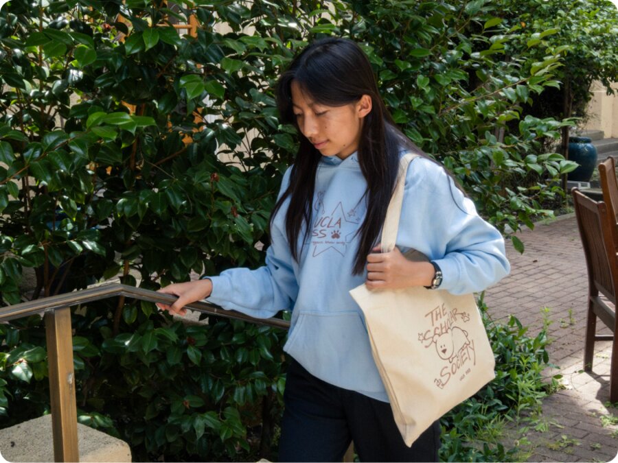 A model carrying the tote on their shoulder beside a garden stairway
